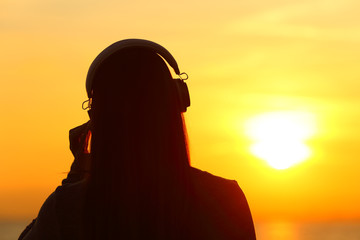 Woman wearing headphones listening to music at sunset