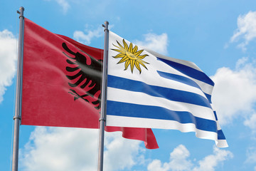 Uruguay and Albania flags waving in the wind against white cloudy blue sky together. Diplomacy concept, international relations.