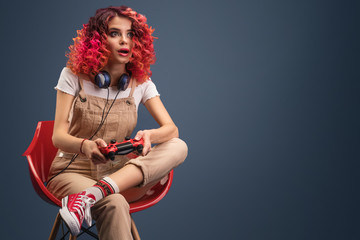 young woman with bright red cyrly hair playing video game.