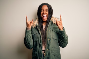 Young african american woman wearing winter parka coat over isolated background shouting with crazy expression doing rock symbol with hands up. Music star. Heavy concept. © Krakenimages.com