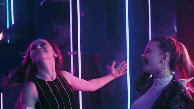 Neon girls. Fun celebration. Amused female friends dancing in confetti rain nightclub purple glow.