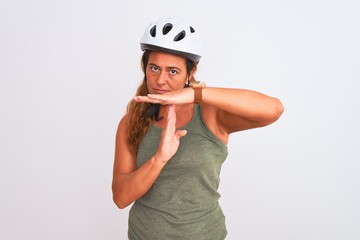 Middle age mature cyclist woman wearing safety helmet over isolated background Doing time out gesture with hands, frustrated and serious face