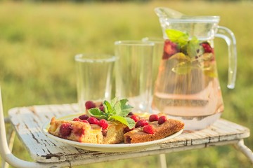 Cake with berries and jug with strawberry mint drink in summer sunny meadow