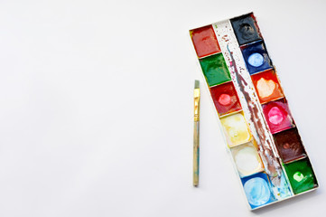 Palette of multicolored used watercolor paints and brush on a white background with copy space, top view, flat lay