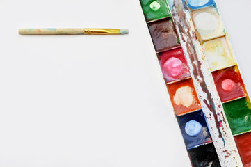Palette of multicolored used watercolor paints and brush on a white background with copy space, top view
