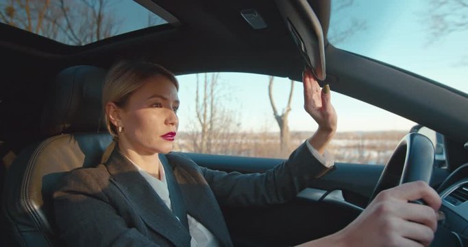 Young pretty blonde Caucasian businesswoman driving an expensive car and taking down protector from the sun.
