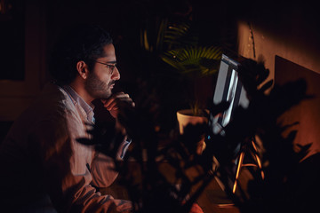 Handsome young doctor is working at late night shift at his office using a computer.