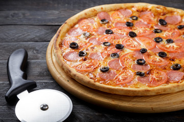 Delicious pizza. Large meat pizza with bacon, sausage, salami, pepperoni and olives. Homemade delicious italian pizza on wooden table for dinner. Italian cuisine.