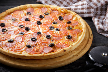 Delicious pizza. Large meat pizza with bacon, sausage, salami, pepperoni and olives. Homemade delicious italian pizza on wooden table for dinner. Italian cuisine.