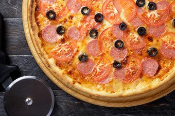 Delicious pizza. Large meat pizza with bacon, sausage, salami, pepperoni and olives. Homemade delicious italian pizza on wooden table for dinner. Italian cuisine.