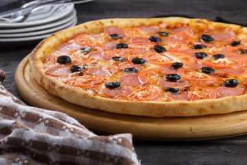 Delicious pizza. Large meat pizza with bacon, sausage, salami, pepperoni and olives. Homemade delicious italian pizza on wooden table for dinner. Italian cuisine.