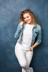 young pretty hipster girl with curly blond hair posing emotonal on blue wall background, lifestyle people concept