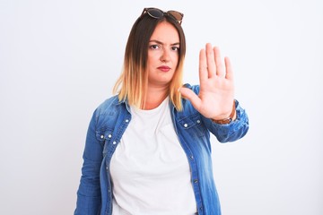 Beautiful woman wearing denim shirt standing over isolated white background doing stop sing with...