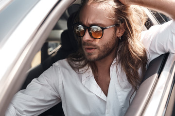 Young adult man sitting in car in sunglasses