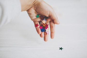 Hand holding colorful sparkling stars decorations on white background. Stylish atmospheric image....
