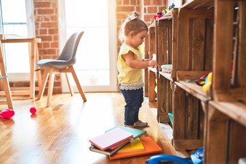 Beautiful toddler standing taking toys of shelving at kindergarten