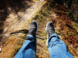 A pair of male legs in jeans and sneakers view from a chair lift on a trail in a mountain valley