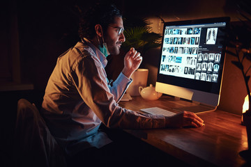 Smart medic in glasses is working with x-ray screens using a computer at dark office.