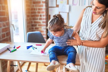 Beautiful toddler sitting on desk crying and young teacher hugging at kindergarten