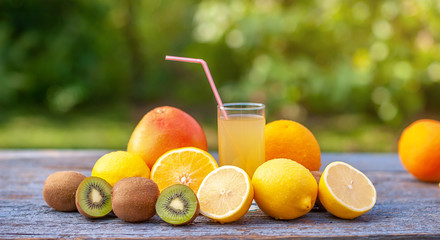 Tasty ripe fruits and a glass of juice on a wooden table in the garden. Useful vitamins. On a green background