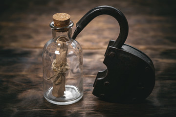 Old parchment scroll in a glass bottle and open padlock on a table.
