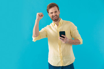 Happy casual man laughing and celebrating, holding a phone