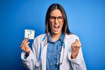 Young beautiful brunette doctor woman holding paper with question mark symbol message annoyed and...