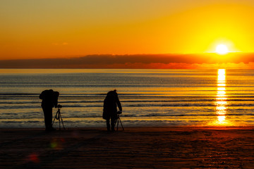 Silhouette of two photographers. A man and a woman are photographing the sunrise on a beach.