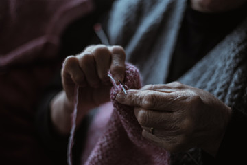 The old woman sits at home and knits garments. Close up.