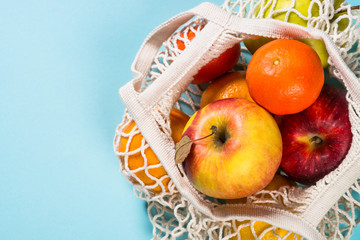 Mesh bag with fruits on color background.