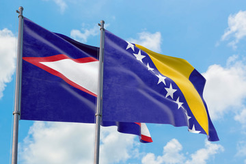 Bosnia Herzegovina and American Samoa flags waving in the wind against white cloudy blue sky...