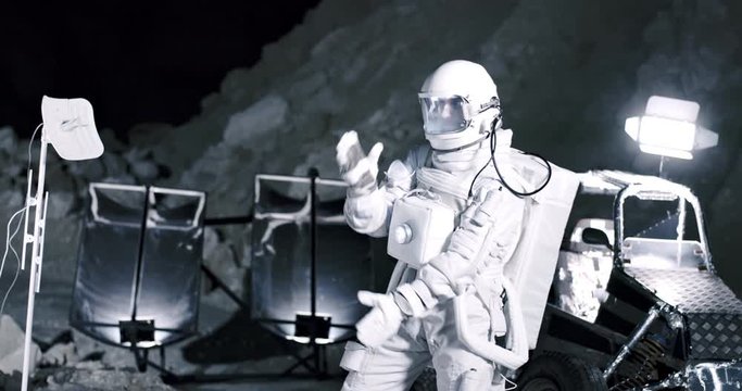 Funny Caucasian spaceman standing at the Moon base in the valley at night and dancing or moving like a robot. Outdoors.
