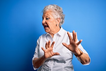 Senior beautiful woman wearing elegant shirt standing over isolated blue background disgusted expression, displeased and fearful doing disgust face because aversion reaction. With hands raised