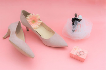 wedding concept. gerbera flower, rings, beige shoes, newlywed figurine on a pink background.
