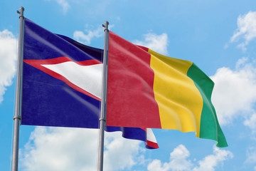 Guinea and American Samoa flags waving in the wind against white cloudy blue sky together. Diplomacy concept, international relations.