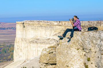 photographer a man with a beard sits on the edge of a rocky mountain with a camera and shoots landscapes