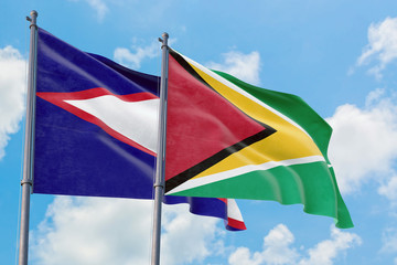 Guyana and American Samoa flags waving in the wind against white cloudy blue sky together. Diplomacy concept, international relations.