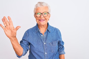 Senior grey-haired woman wearing denim shirt and glasses over isolated white background showing and pointing up with fingers number five while smiling confident and happy.