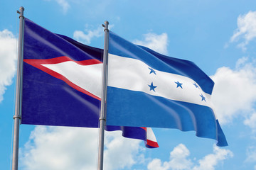 Honduras and American Samoa flags waving in the wind against white cloudy blue sky together. Diplomacy concept, international relations.