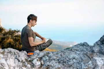 Fototapeta na wymiar Young Man sitting on rocks and Painting Mountains and sea