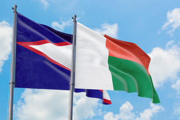 Madagascar and American Samoa flags waving in the wind against white cloudy blue sky together. Diplomacy concept, international relations.