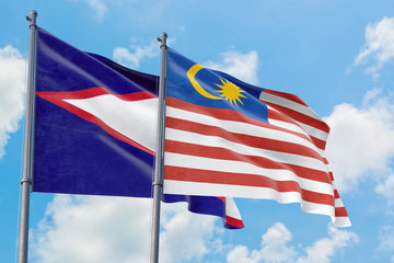 Malaysia and American Samoa flags waving in the wind against white cloudy blue sky together. Diplomacy concept, international relations.