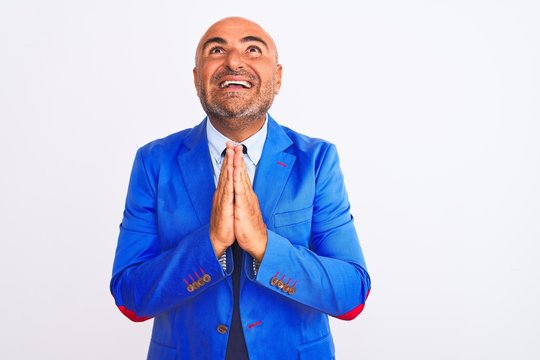Middle age businessman wearing suit standing over isolated white background praying with hands together asking for forgiveness smiling confident.