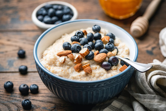 Oatmeal porridge with blueberries, almonds in bowl on wooden table background. Healthy breakfast food
