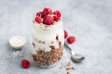Yogurt with granola and raspberries in jar on concrete background. Healthy breakfast or snack on the go - Powered by Adobe