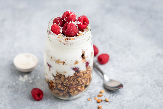 Yogurt with granola and raspberries in jar on concrete background. Healthy breakfast or snack on the go