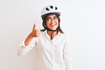 Beautiful businesswoman wearing glasses and bike helmet over isolated white background doing happy thumbs up gesture with hand. Approving expression looking at the camera showing success.