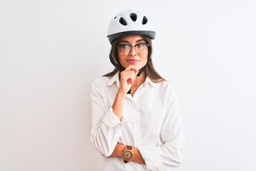 Beautiful businesswoman wearing glasses and bike helmet over isolated white background looking confident at the camera with smile with crossed arms and hand raised on chin. Thinking positive.
