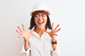 Young beautiful architect woman wearing helmet and glasses over isolated white background celebrating crazy and amazed for success with arms raised and open eyes screaming excited. Winner concept