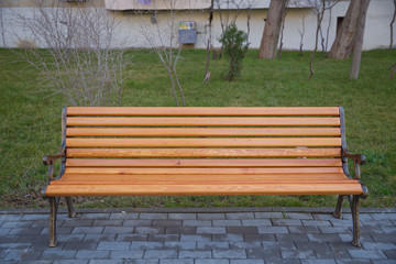Wood exterior material. Wood material details. Blank Old bench in a shady area of the garden or the park,outdoor. Shaded wood park bench surrounded by greenery . Empty Park wooden bench Closeup view.
